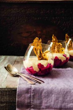 three glasses filled with dessert sitting on top of a wooden table next to silverware