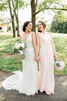 two women standing next to each other in front of some trees and grass holding hands