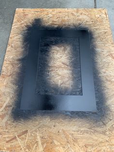 a square shaped object sitting on top of some plywood planks with the shadow of a person in the center