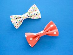 two small bows with polka dots on them are sitting on a blue surface, one is red and the other is white