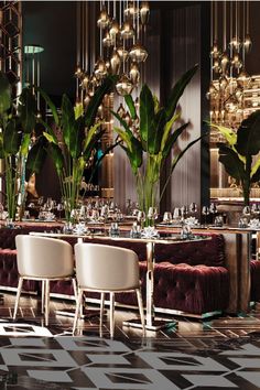 the dining room is set up for an event with tall plants and chandeliers hanging from the ceiling