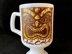 a white coffee cup with an image of a tiki mask on it's side