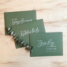 three green envelopes with calligraphy on them sitting on a wooden table next to each other