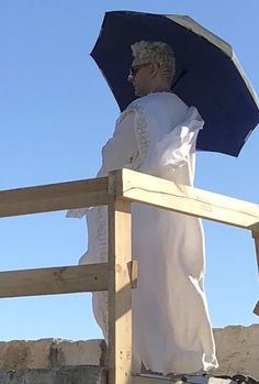 a man standing on top of a wooden fence holding an umbrella over his head and looking at the sky