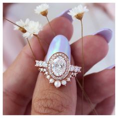 a close up of a person holding a ring on their finger with flowers in the background