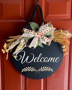 a welcome sign hanging on the front door with a bow and some fall decorations around it