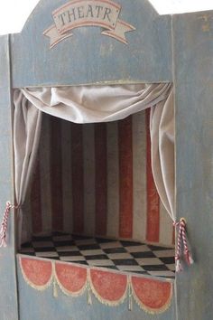 an old wooden puppet house with curtains and checkered flooring on the outside wall