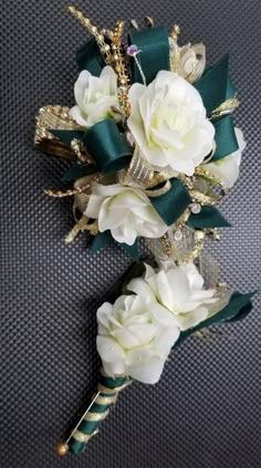 two white flowers with green ribbons on a gray surface, one is gold and the other is dark green