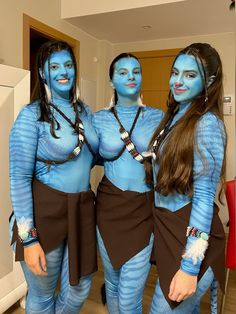 three women dressed in blue and brown posing for the camera with their faces painted like avatars