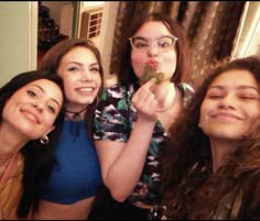 four women are posing for the camera with food in their hands and one is holding something up to her mouth