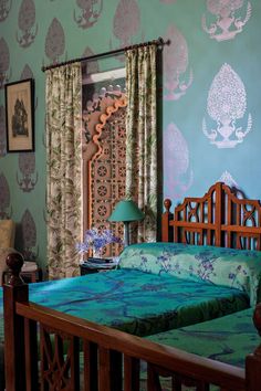 two beds in a room with blue wallpaper and wooden headboards, one has a green comforter on it