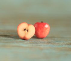 two pieces of fruit sitting next to each other on a wooden table with one apple cut in half