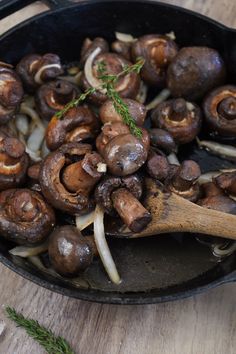 mushrooms and onions cooking in a skillet with a wooden spoon next to them on a table