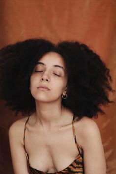 a woman with her eyes closed wearing a brown and black dress is sitting in front of an orange background