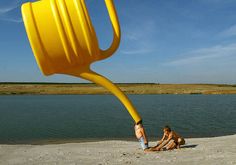 two people on the beach playing with a giant yellow object in front of some water