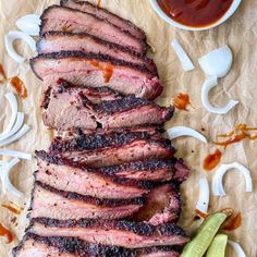 sliced steak on parchment paper with sauces and pickles next to it, ready to be eaten