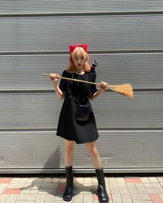 a woman dressed in black holding a broom and wearing a red bow on her head