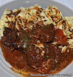 a white plate topped with pasta and meat covered in gravy on top of a table