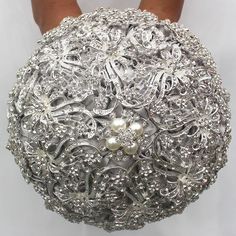 a close up of a person's hand holding a silver brooch with pearls