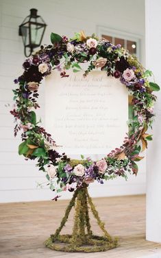 a wedding ceremony sign with flowers and greenery on it is displayed in front of a white house