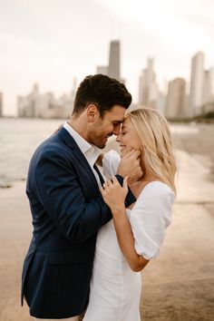 a man and woman standing next to each other in front of the ocean with city skyline behind them