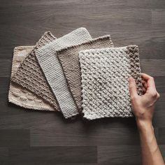 a person is holding four pieces of knitted cloth on a wooden floor with their hands