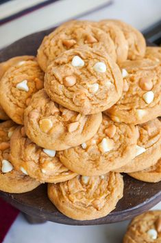 a pile of cookies sitting on top of a wooden plate filled with white chocolate chips