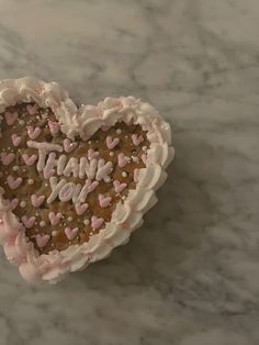 a heart shaped cake sitting on top of a marble counter topped with white frosting and pink sprinkles