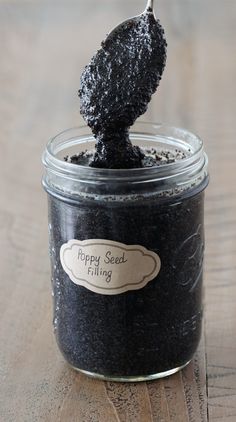 a jar filled with black stuff sitting on top of a wooden table next to a spoon