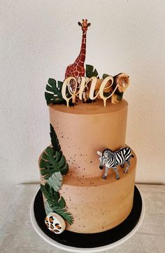 a three tiered cake with an animal topper and jungle decorations on the side