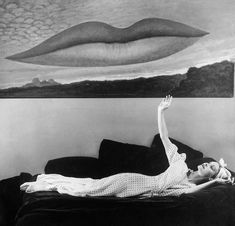 a black and white photo of a woman laying on a couch with her arms in the air