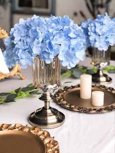 blue hydrangeas in glass vases sitting on top of a white table cloth