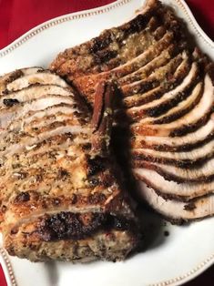 two pieces of meat on a white plate with red table cloth and fork in the background