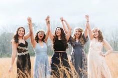 four women standing in a field holding their arms up and smiling at the camera with one woman wearing a flower crown