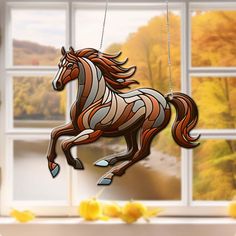 a stained glass horse ornament hanging in front of a window with fall foliage