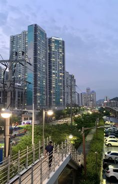 a man walking across a bridge over a river next to tall buildings in a city