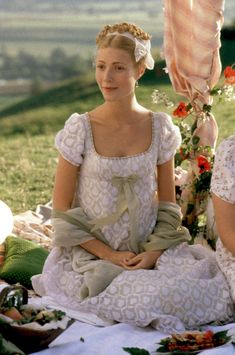 two women sitting on the ground in dresses and bonnets, one wearing a flowered headband