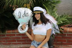 a woman in shorts and a white shirt holding a balloon with the word i do written on it