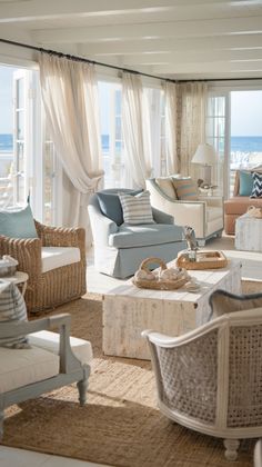 a living room filled with lots of furniture next to an ocean side window covered in white curtains