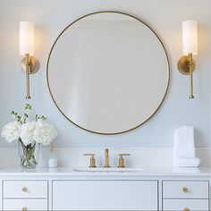 a bathroom vanity with a round mirror above it and flowers in vase on the counter