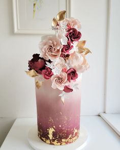 there is a pink and gold cake with flowers on the top, sitting on a white table