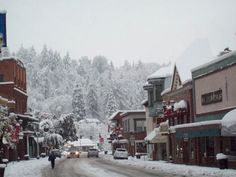 a snowy street with cars parked on the side and people walking down the road in the distance