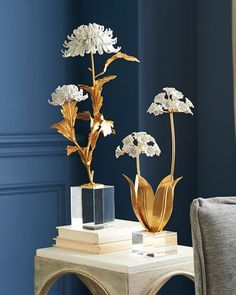 two vases with flowers are sitting on a small table in front of a blue wall