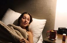 a woman laying in bed under a blanket next to a coffee cup and camera on the table