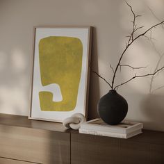 a black vase sitting on top of a wooden shelf next to a framed art piece