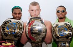 three men standing next to each other holding up their wrestling belts