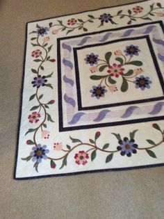 a quilted table runner with flowers and leaves in the center on a beige floor