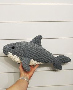 a hand holding a stuffed shark toy in front of a white wall with planks