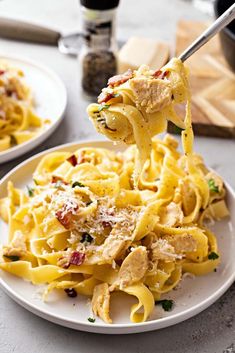 a fork full of pasta with chicken and parmesan cheese on the top is being lifted from a white plate