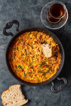 a pan filled with food next to bread and a glass of wine on a table